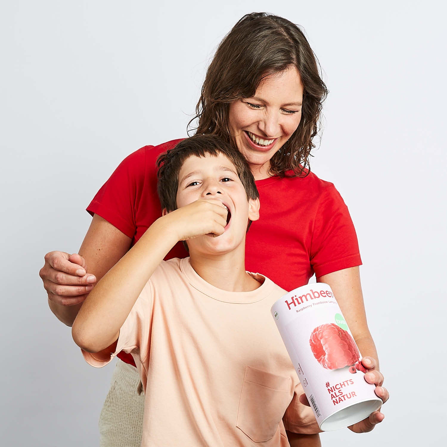 Mama und Sohn lachen und probieren buah gefriergetrocknete Himbeeren aus einer Dose buah Himbeeren
