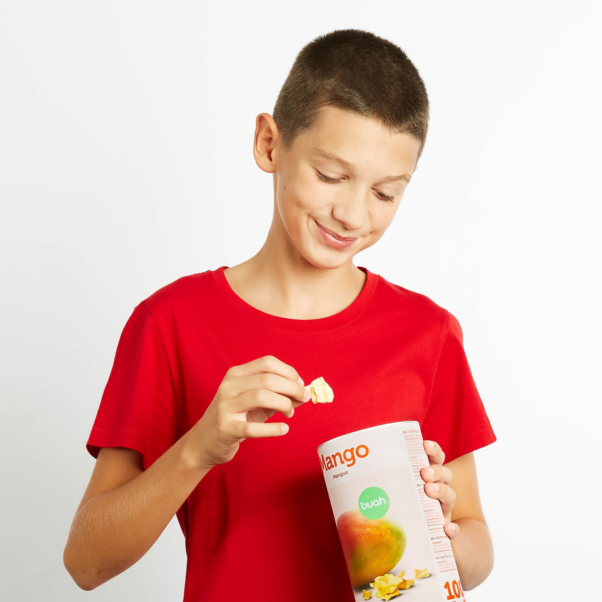 Junge in rotem Shirt hat eine Dose buah gefriergetrocknete Mango in der Hand und isst daraus