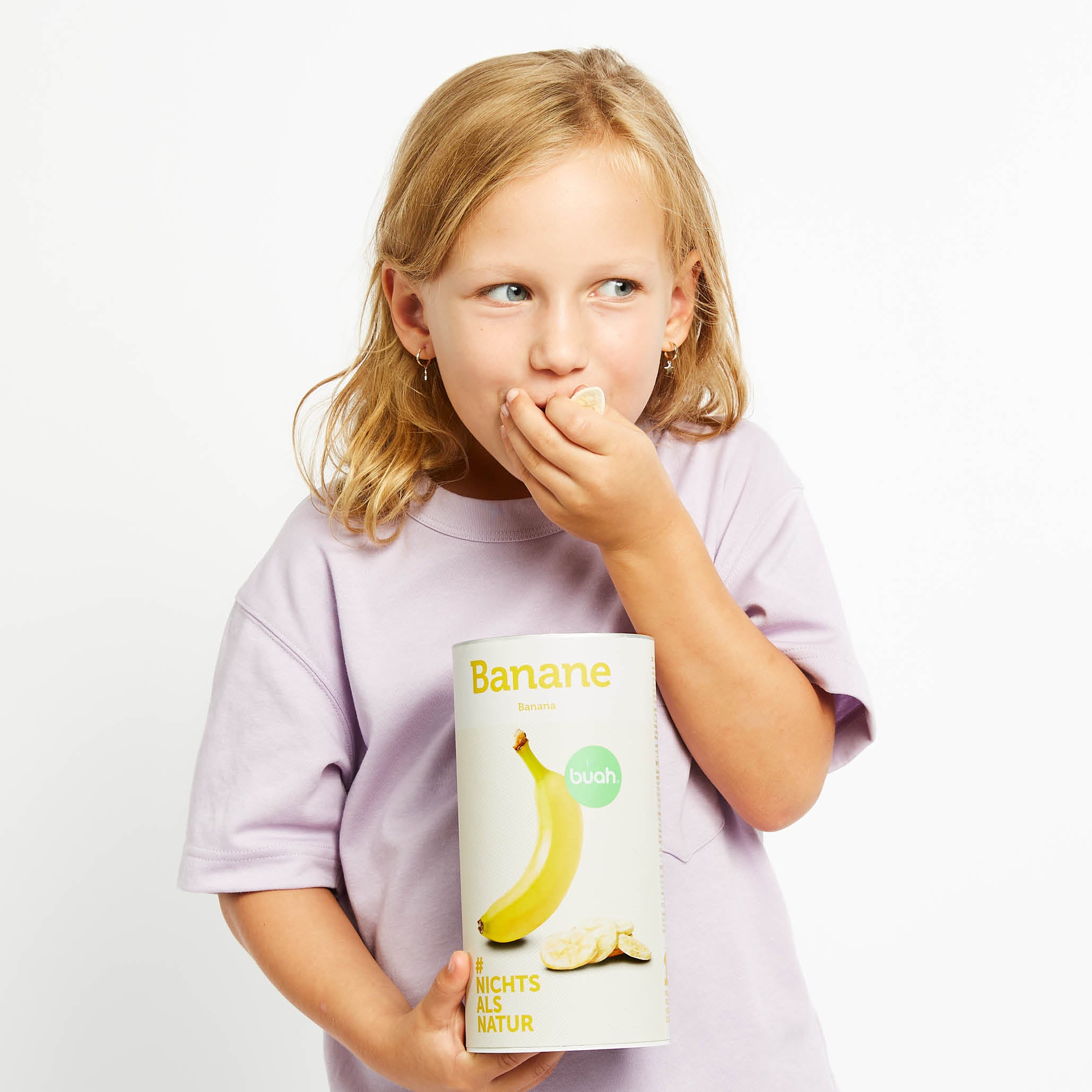 Junges Maedchen in lila Tshirt lacht und isst buah gefriergetrocknete Bananen aus einer Dose buah Bananen in Ihrer Hand