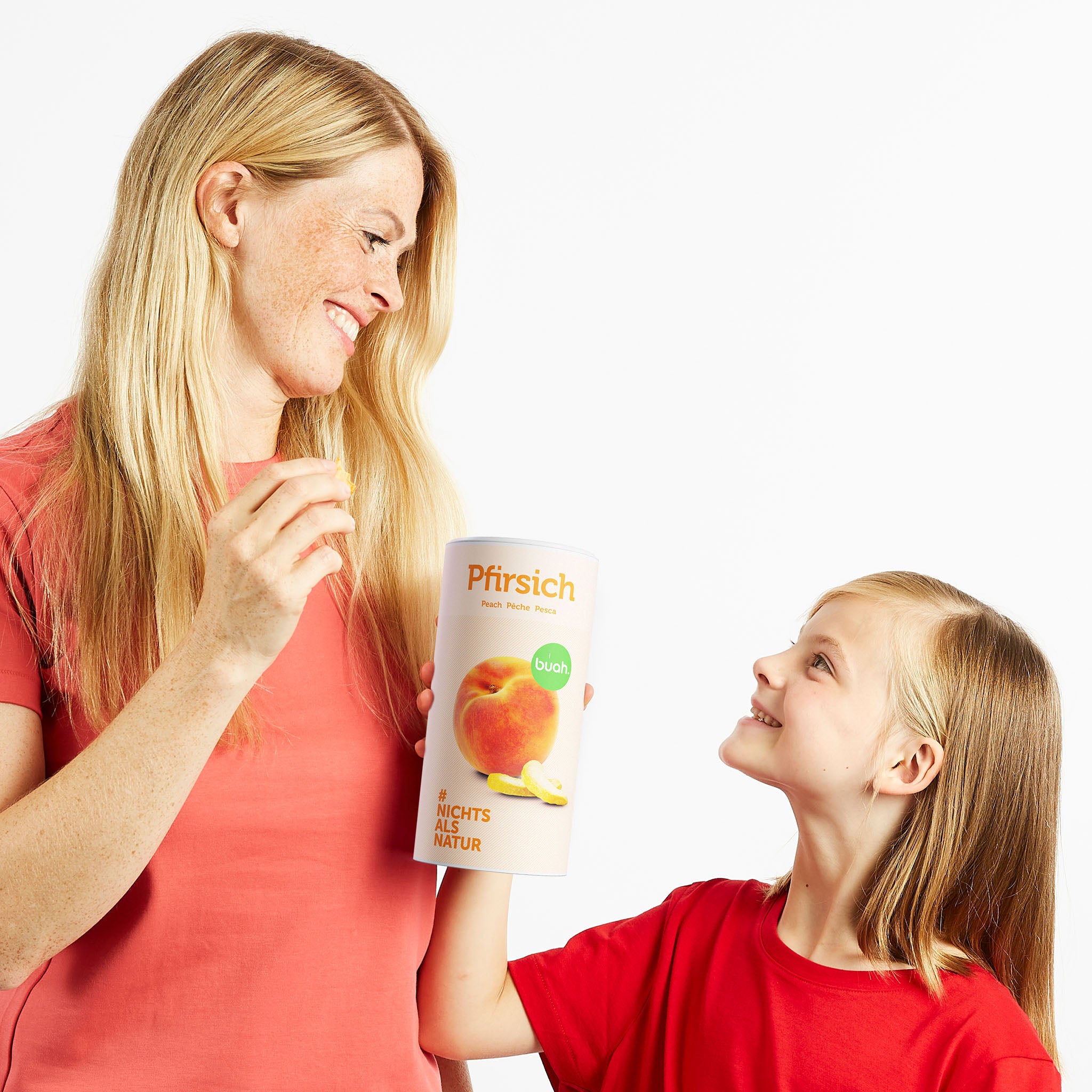 Mama und Tochter schauen sich an und halten eine Dose buah gefriergetrockneter Pfirsich in der Hand