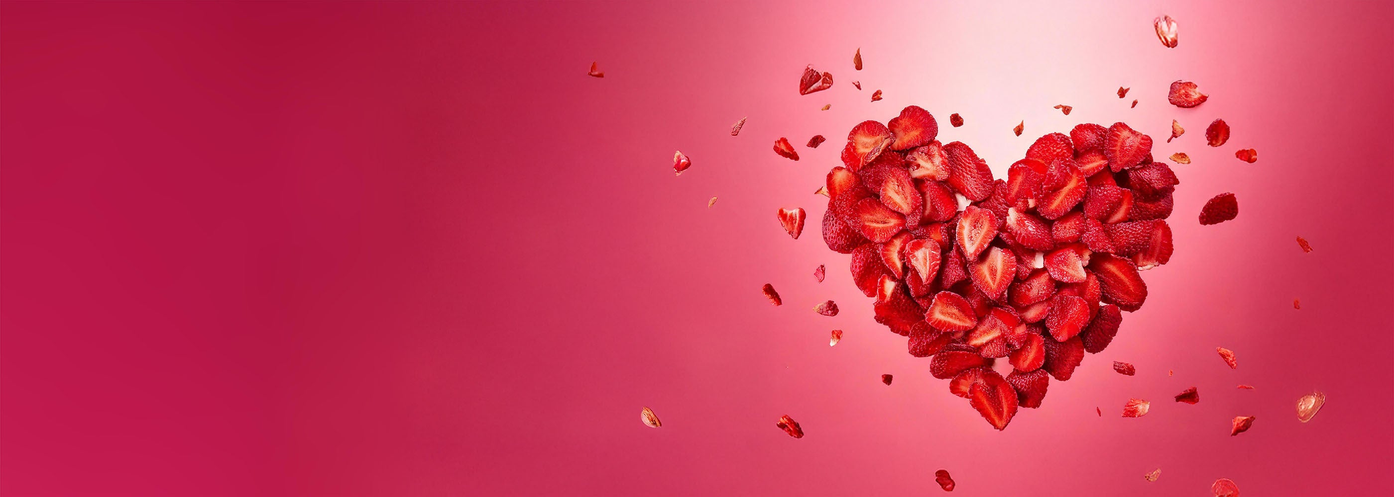 Explodierendes Valentinstag Herz aus roten buah gefriergetrockneten Erdbeeren vor rotem Hintergrund mit der Message Liebe verschenken.