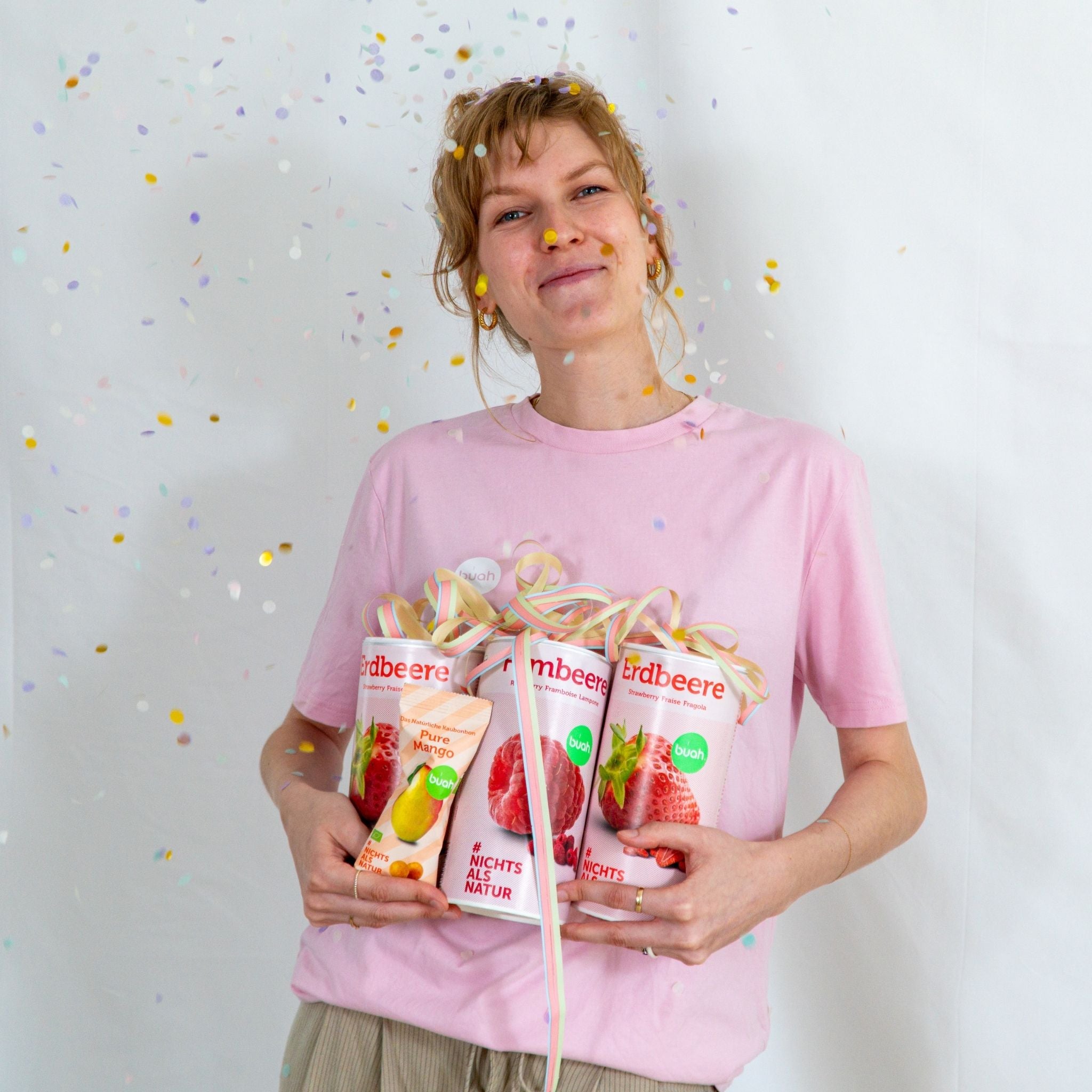 Sarah von buah im rosa buah Shirt mit buah gefriergetrockneten Fruechten in der Dose im Arm - Konfetti und Luftschlangen im Hintergrund fuer den buah Birthday