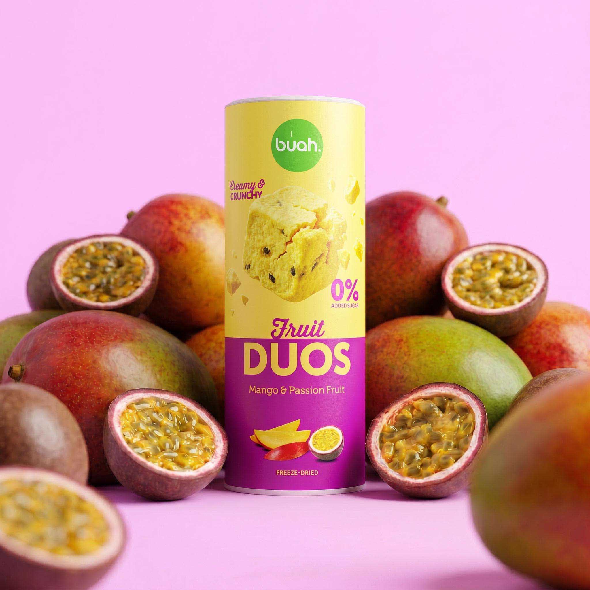Eine hohe Slim-Dose buah Fruit DUOS Mango & Maracuja steht inmitten von frischen, ganzen Mangos und aufgeschnittenen Maracujas vor einem rosafarbenen Hintergrund.