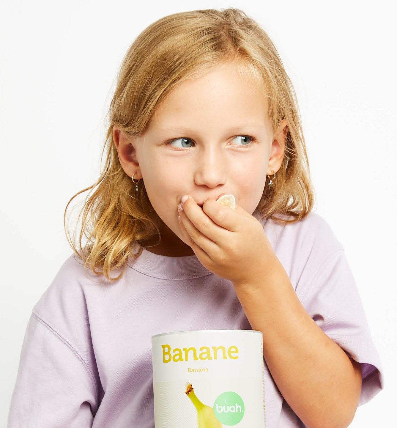 Junges Kind mit lila Shirt isst buah gefriergetrocknete Bananen aus einer Dose Banane