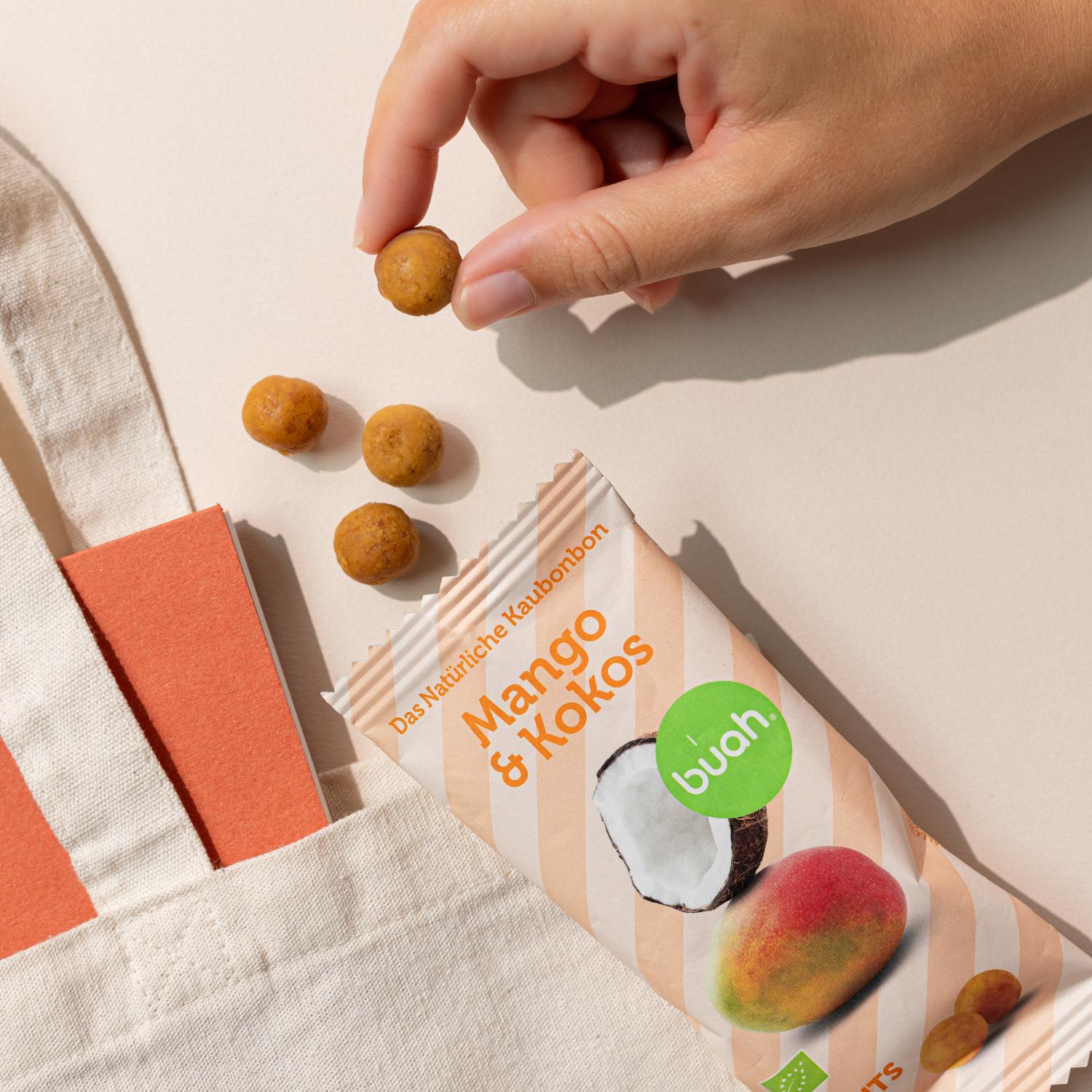 Mango-Kokos Kaubonbon wird von Hand aus Verpackung genommen, Tasche im Hintergrund