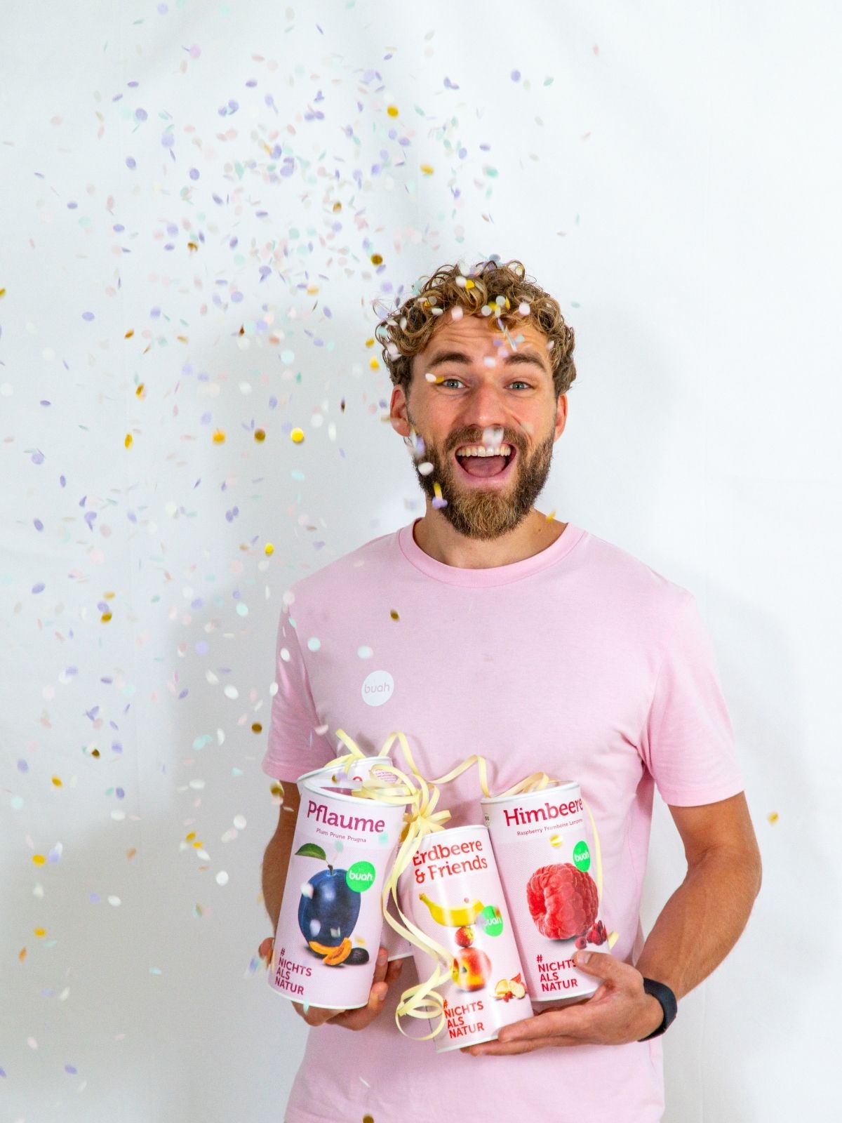 Daniel Gruender von buah in rosa buah Shirt mit buah gefriergetrockneten Fruechten in der Dose im Arm - Konfetti und Luftschlangen im Hintergrund  fuer den buah Birthday
