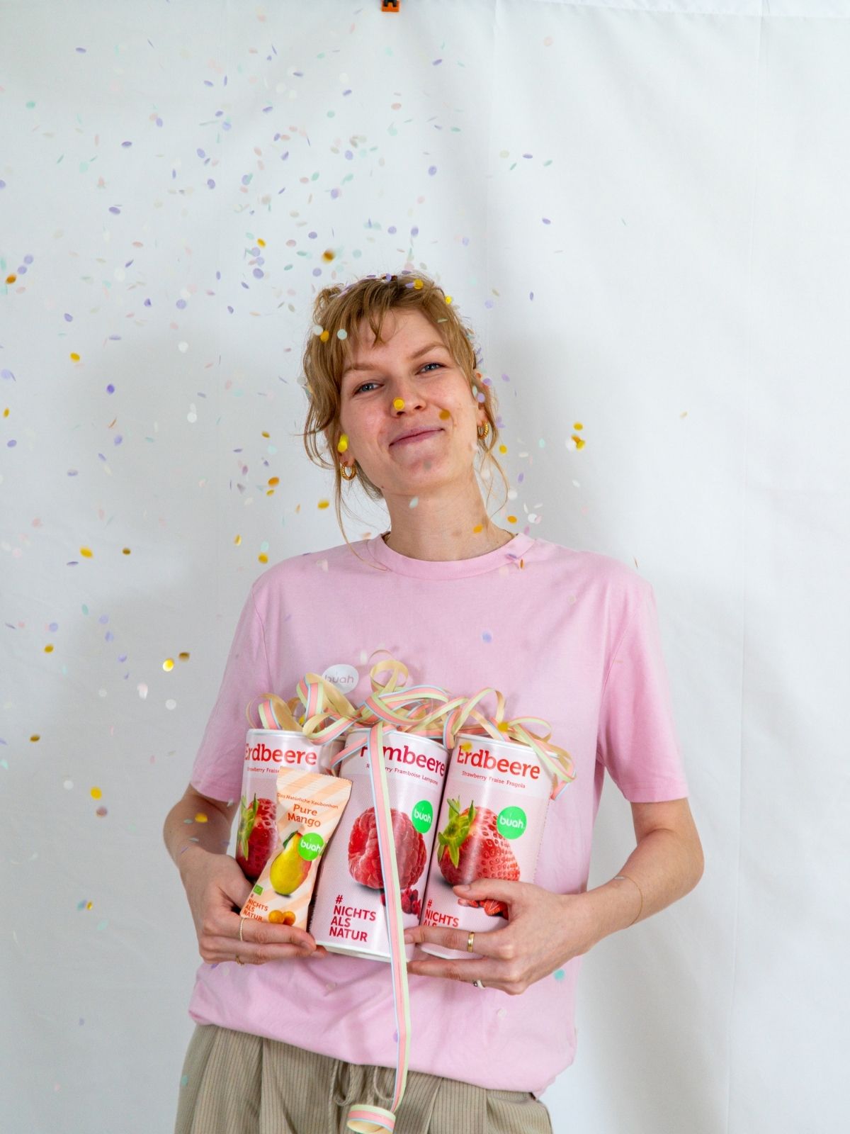 Sarah von buah im rosa buah Shirt mit buah gefriergetrockneten Fruechten in der Dose im Arm - Konfetti und Luftschlangen im Hintergrund  fuer den buah Birthday