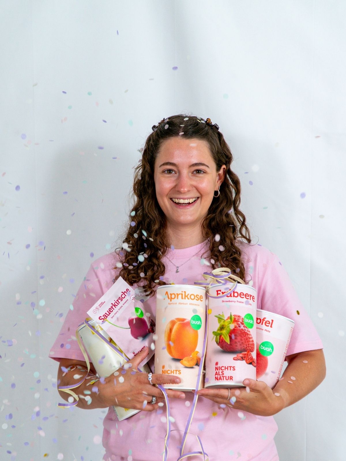 Vanessa von buah im rosa buah Shirt mit buah gefriergetrockneten Fruechten in der Dose im Arm - Konfetti und Luftschlangen im Hintergrund  fuer den buah Birthday