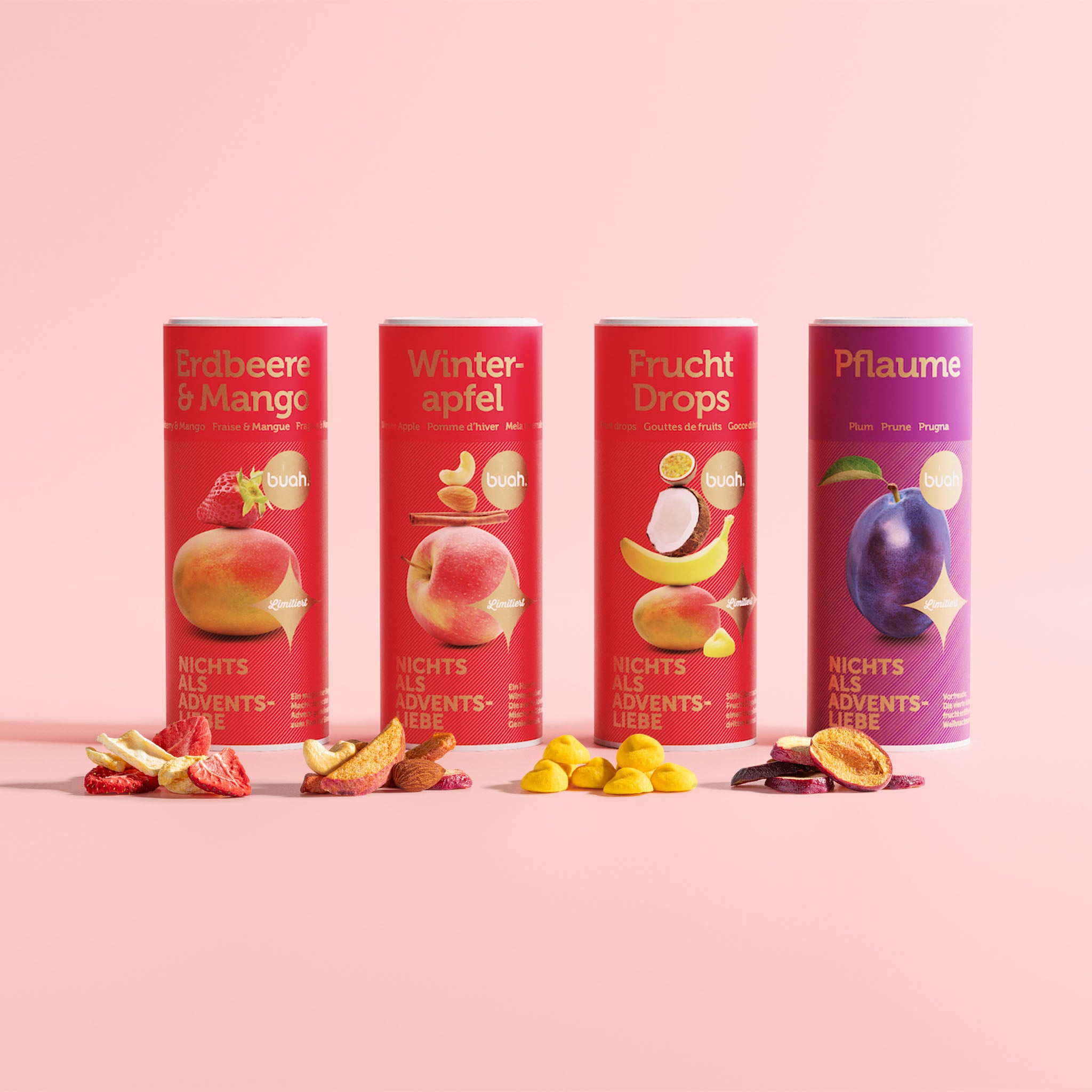 buah Adventskalender Special Edition Dosen in 4 neuen Sorten mit roter und goldener Verpackung stehen nebeneinander mit Fruechten vor den Dosen liegend