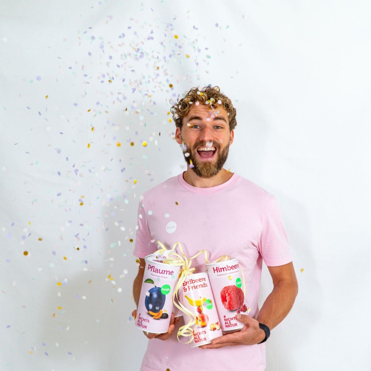 Daniel Gruender von buah in rosa buah Shirt mit buah gefriergetrockneten Fruechten in der Dose im Arm - Konfetti und Luftschlangen im Hintergrund  fuer den buah Birthday