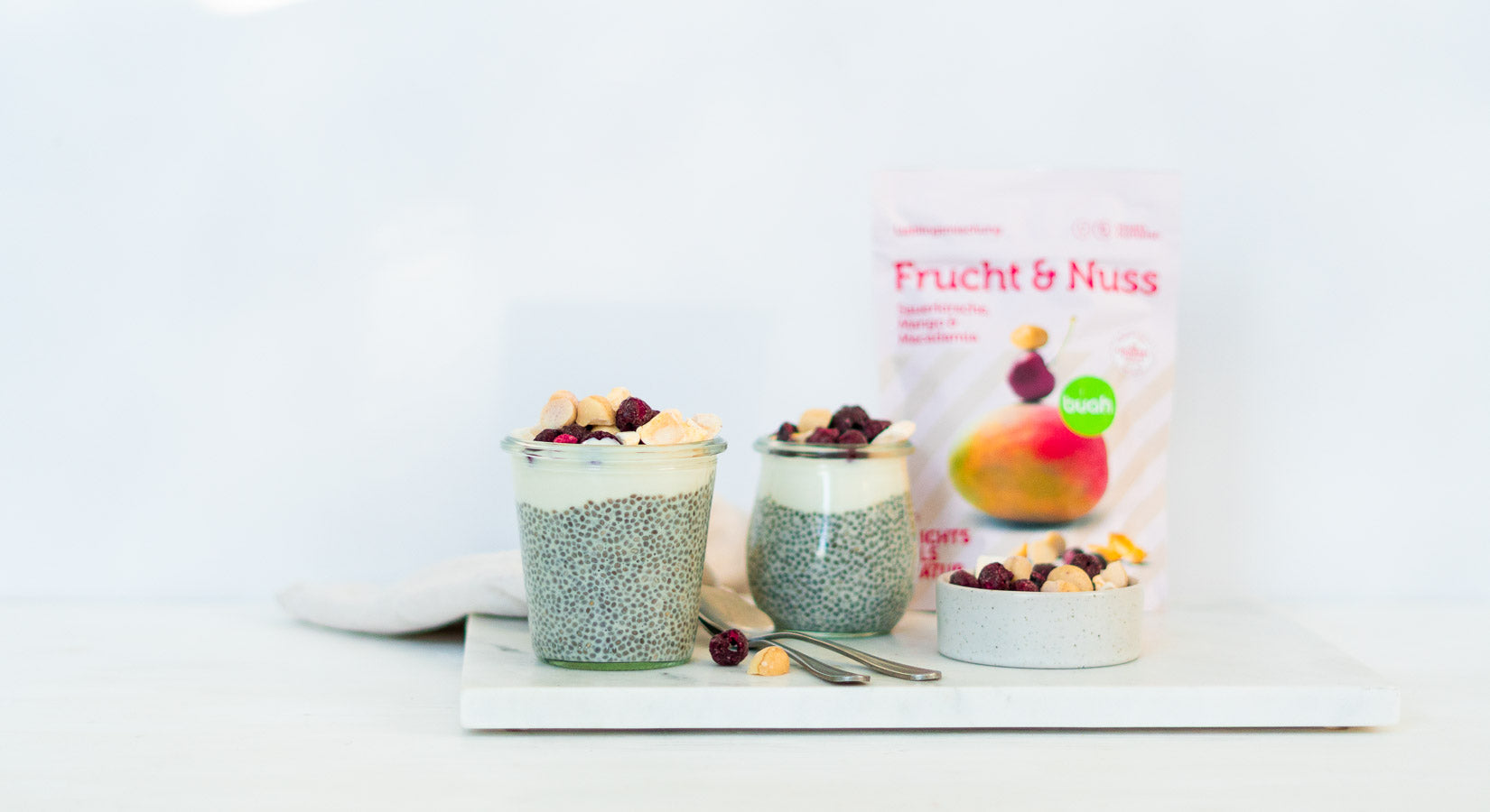 Chia Pudding in zwei kleinen Dessert Gläschen mit Joghurt und buah Frucht & Nuss Sauerkirsche, Mango und Macadamia als Topping