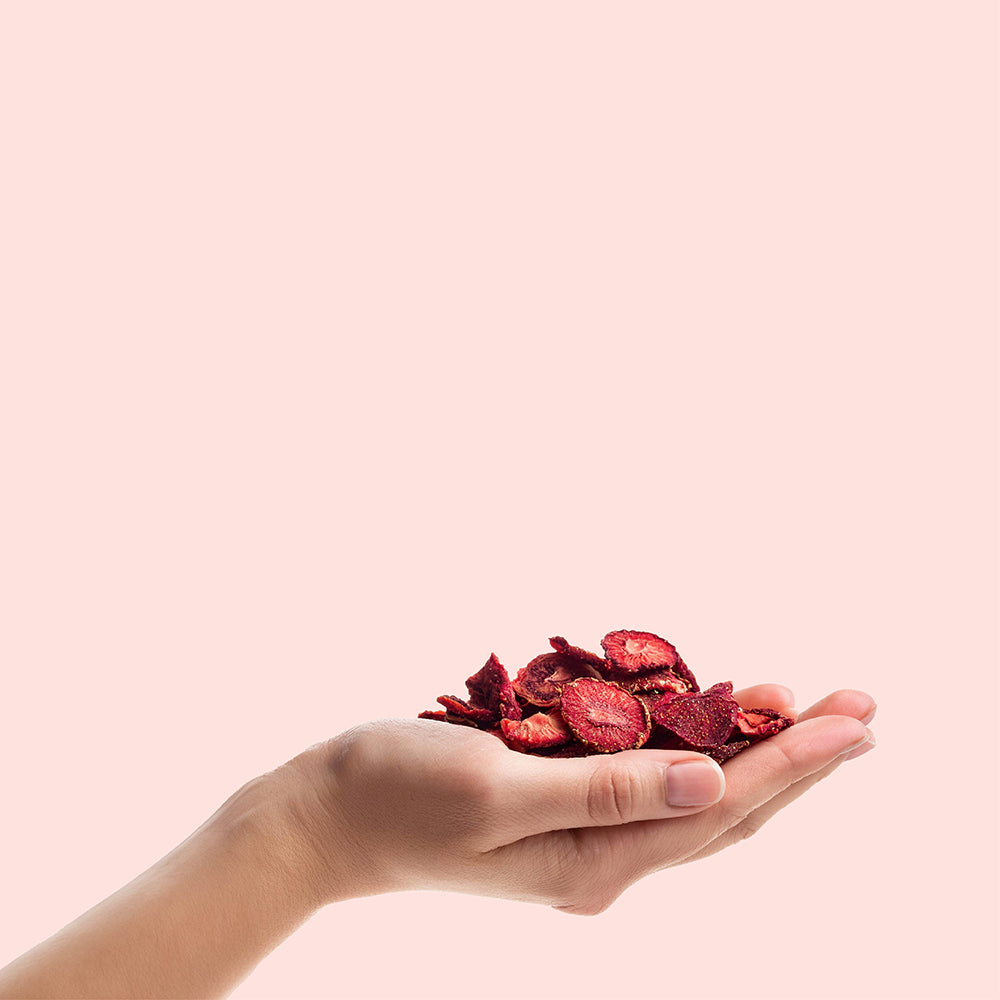 buah gefriergetrocknete Erdbeeren liegen in einer ausgestreckten Hand vor rosa Hintergrund 