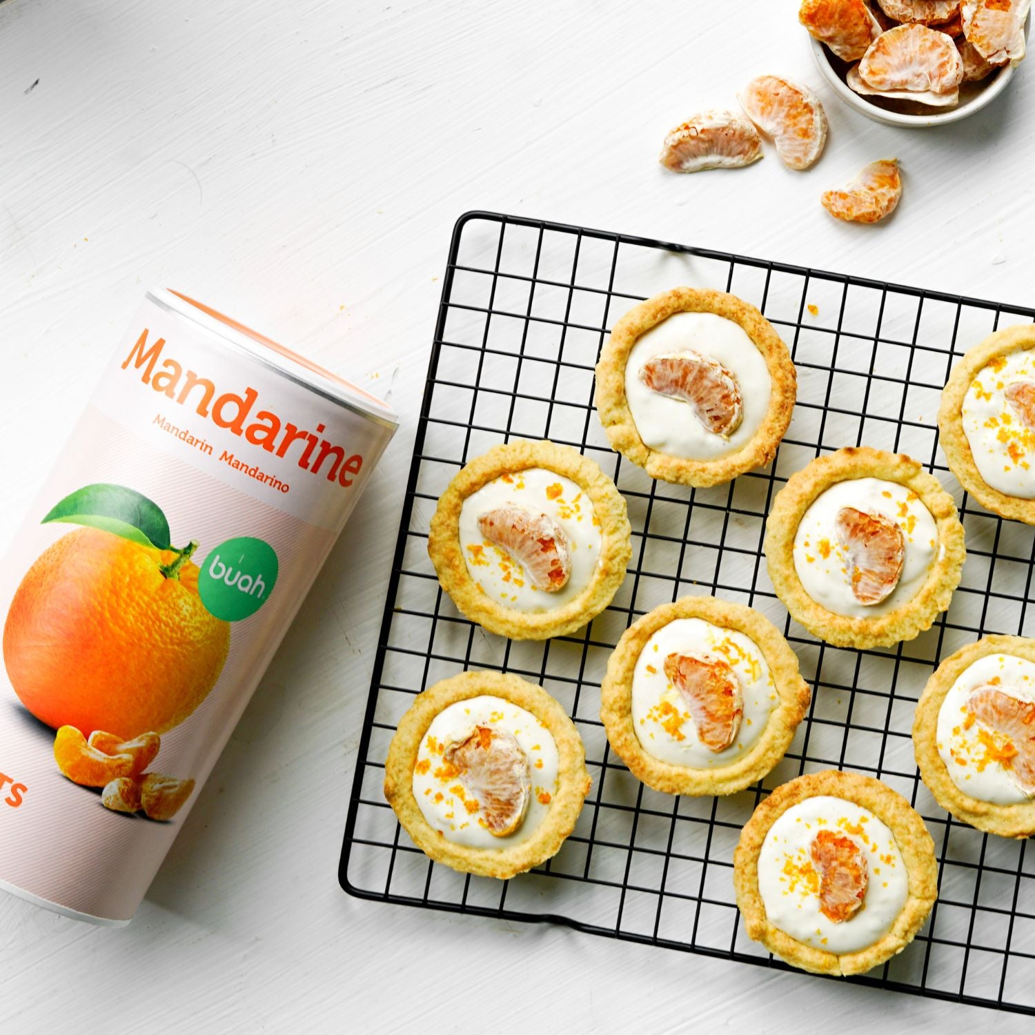 Tartlets mit Creme und buah gefriergetrockneter Mandarine liegen auf einem Backgitter, daneben eine Dose buah Mandarine 