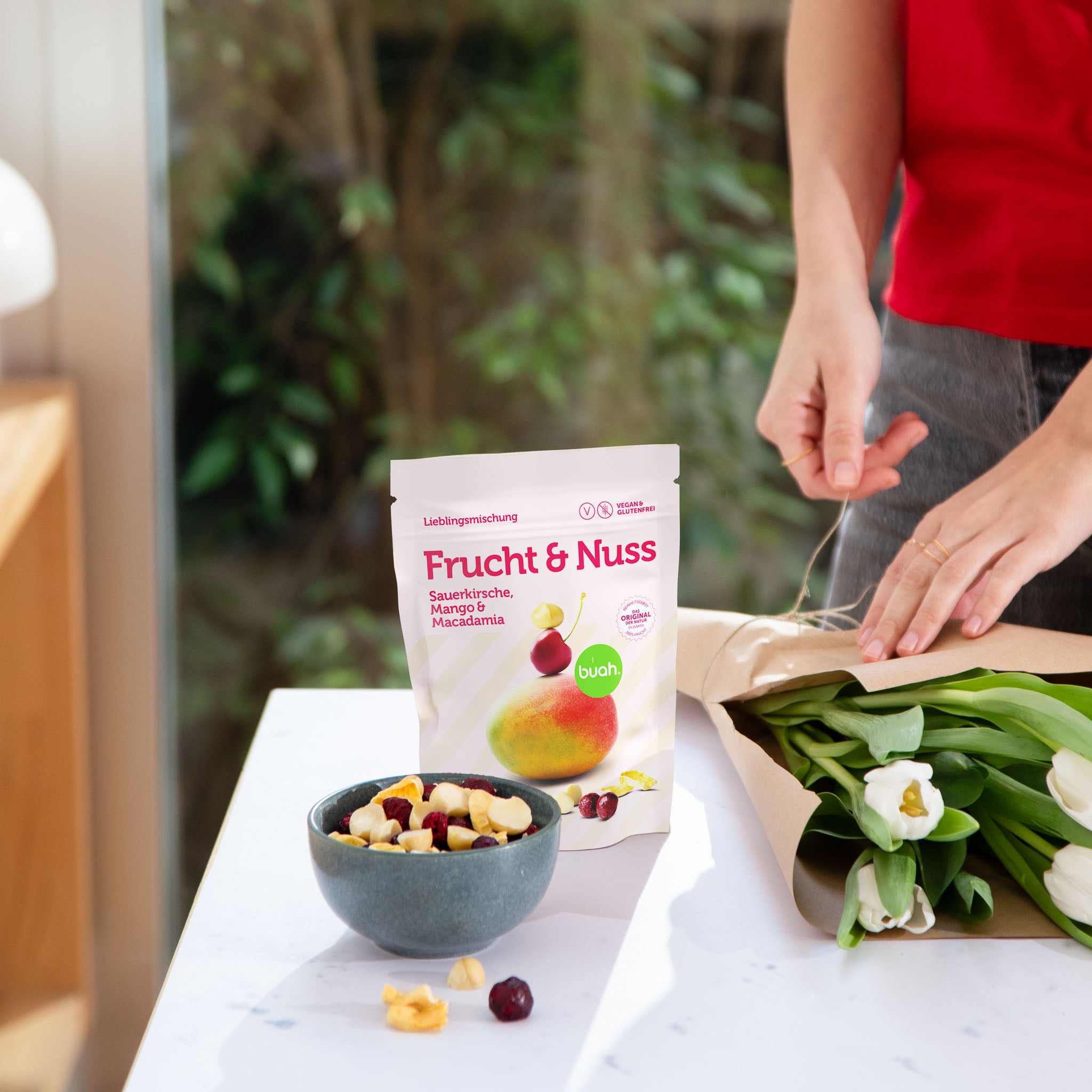 buah Frucht & Nuss Mischung mit Sauerkirsche Mango und Macadamia steht auf einem Tisch neben einem Bund frischer Frühlingsblumen 