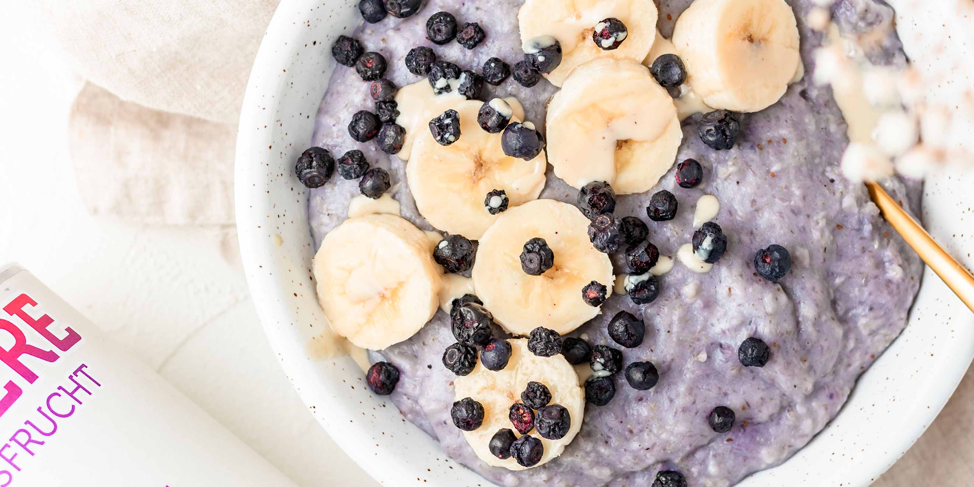 Porridge in einer weißen Schale mit Banane und buah Blaubeeren als Topping 