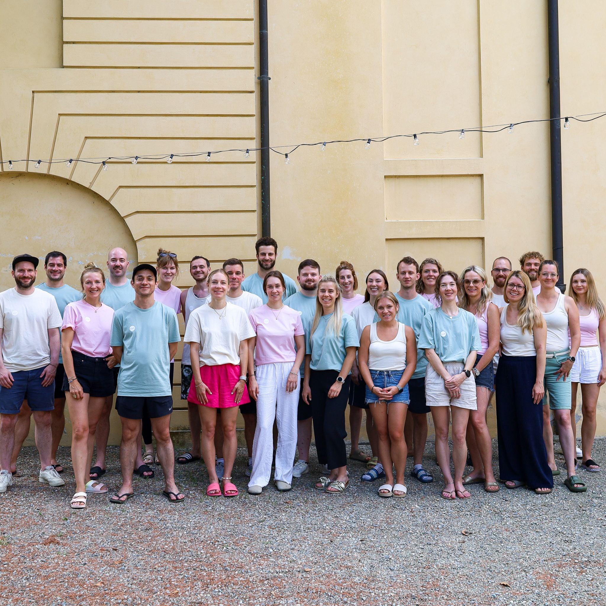 Bild des buah Teams vor einer gelben Wand, viele Frauen und Maenner in Pastell  Farben Shirts, im Sommer