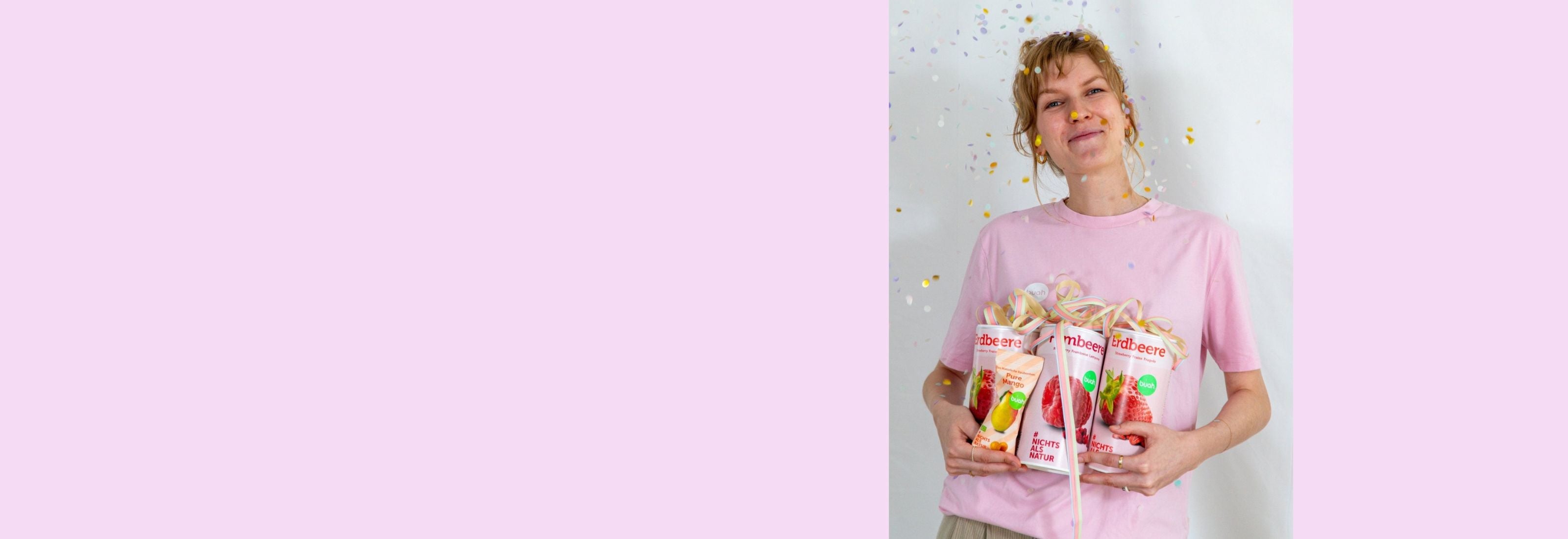 Sarah von buah im rosa buah Shirt mit buah gefriergetrockneten Fruechten in der Dose im Arm - Konfetti und Luftschlangen vor rosa Hintergrund
