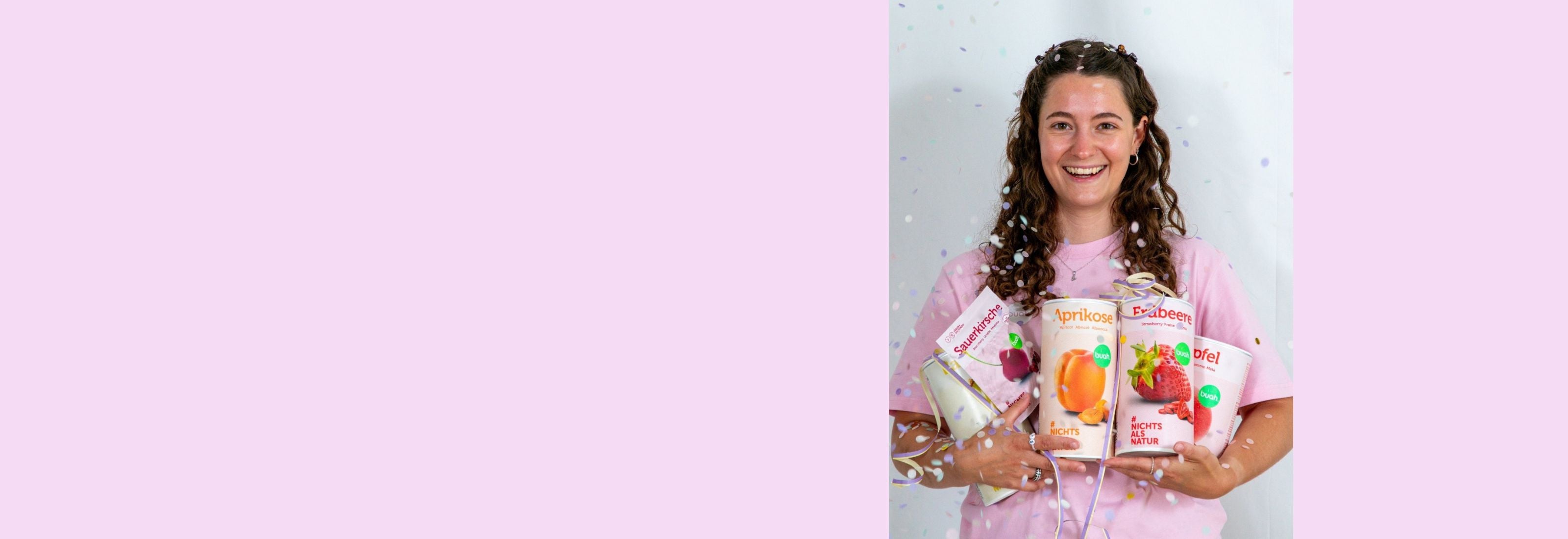 Vanessa von buah im rosa buah Shirt mit buah gefriergetrockneten Fruechten in der Dose im Arm - Konfetti und Luftschlangen vor rosa Hintergrund