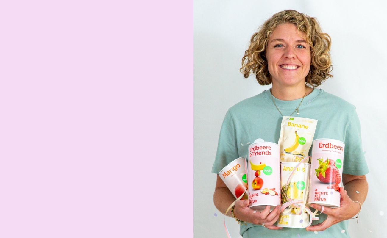Jessica Gruenderin von buah in gruenem buah Shirt mit buah gefriergetrockneten Fruechten in der Dose im Arm - Konfetti und Luftschlangen vor rosa Hintergrund  