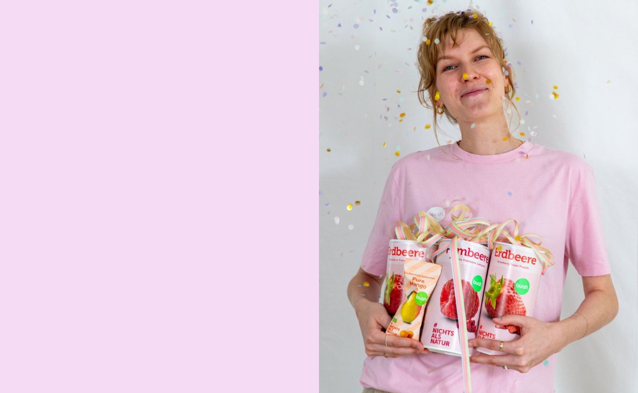 Sarah von buah im rosa buah Shirt mit buah gefriergetrockneten Fruechten in der Dose im Arm - Konfetti und Luftschlangen vor rosa Hintergrund