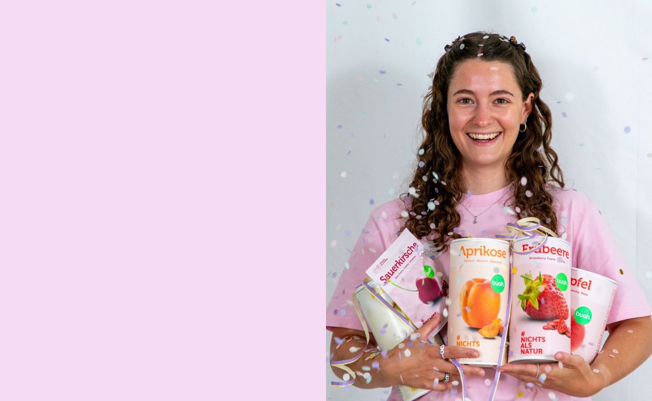 Vanessa von buah im rosa buah Shirt mit buah gefriergetrockneten Fruechten in der Dose im Arm - Konfetti und Luftschlangen vor rosa Hintergrund